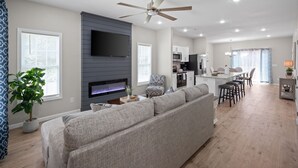 Ein modernes Wohnzimmer mit grauem Sofa, einem flachbildfernseher an der Wand und einem Deckenventilator.