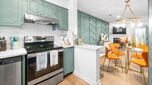 Une cuisine moderne avec des armoires de couleur turquoise, une cuisinière en acier inoxydable et un coin repas avec des chaises orange et une table en verre.