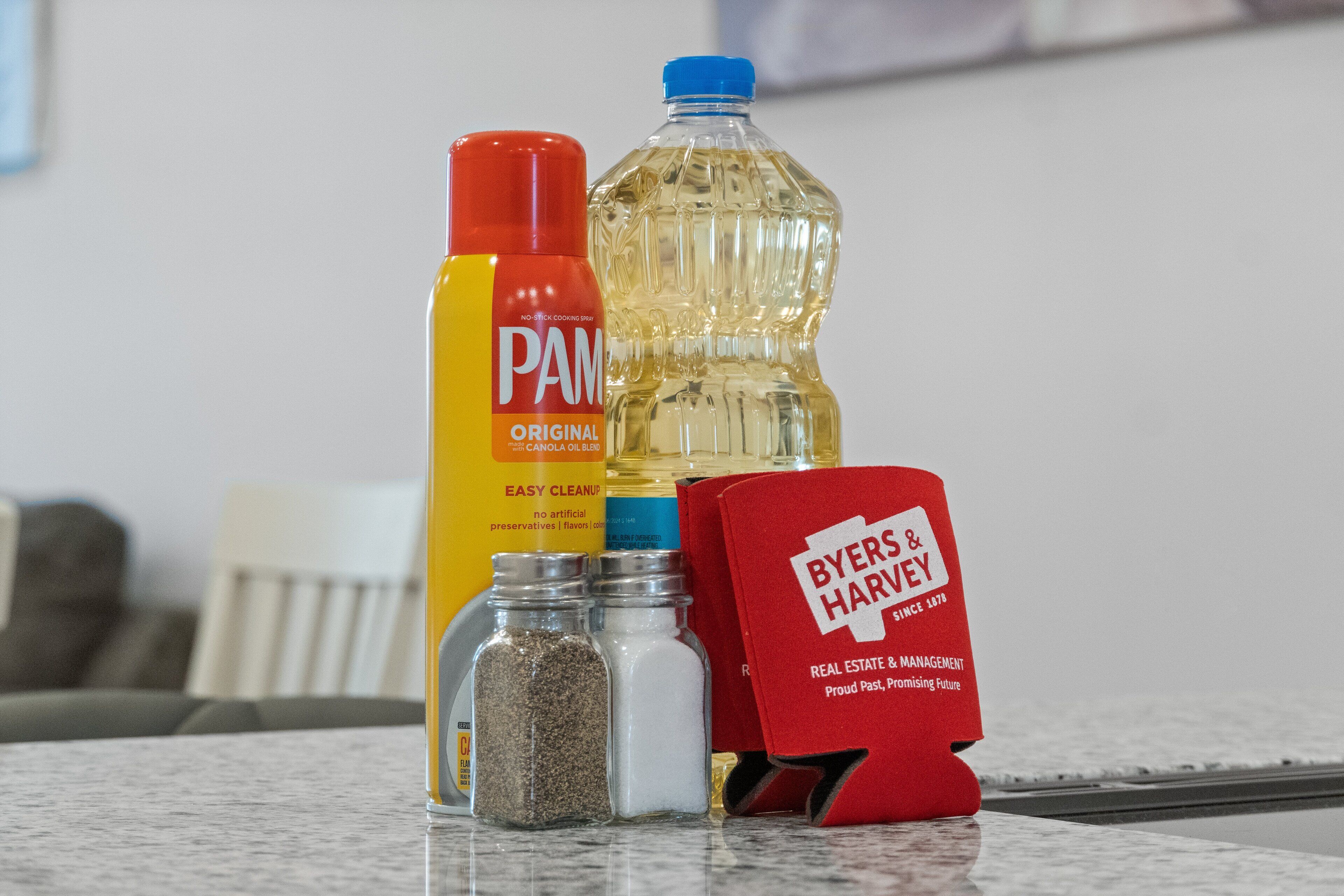 A kitchen counter with a bottle of PAM dish soap, a large bottle of cooking oil, two spice jars, and a red box labeled BYERS & HARVEY.