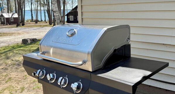 A stainless steel grill with four control knobs and a digital display, positioned outdoors in front of a house.