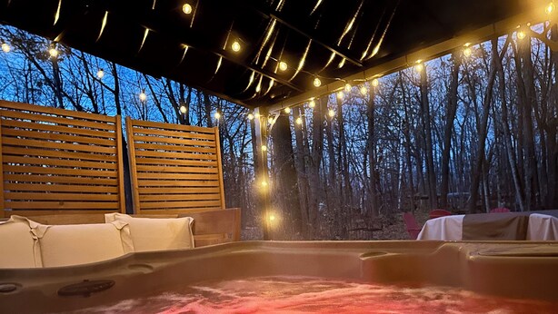 Een hottubgedeelte met houten banken en lichtjes, omringd door bomen.
