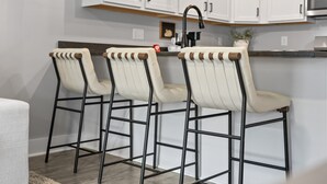 Une cuisine avec des meubles blancs, un robinet noir et trois tabourets de bar dotés d’assises en bois et de structures métalliques.