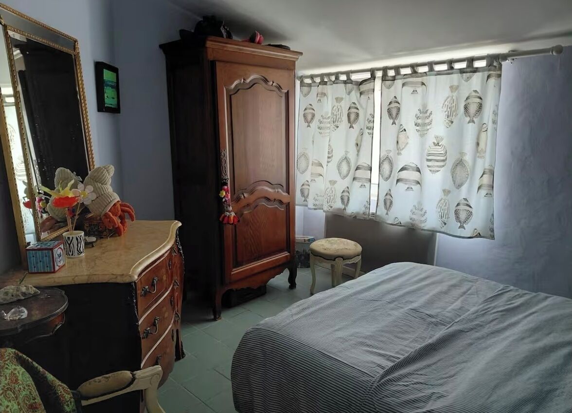 A bedroom with a bed, a dresser, a mirror, and a window with curtains.
