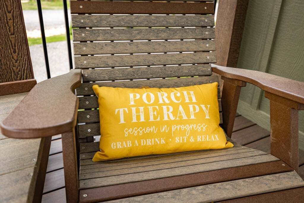 En trästol med en gul kudde där det står: ”PORCH THERAPY – session pågår. Ta något att dricka, sitt ner och koppla av”.