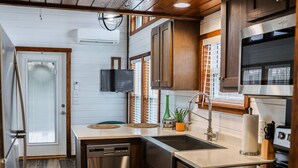 A compact kitchen with wooden flooring, stainless steel appliances, and a built-in oven. - The Family Truckster (Dover)