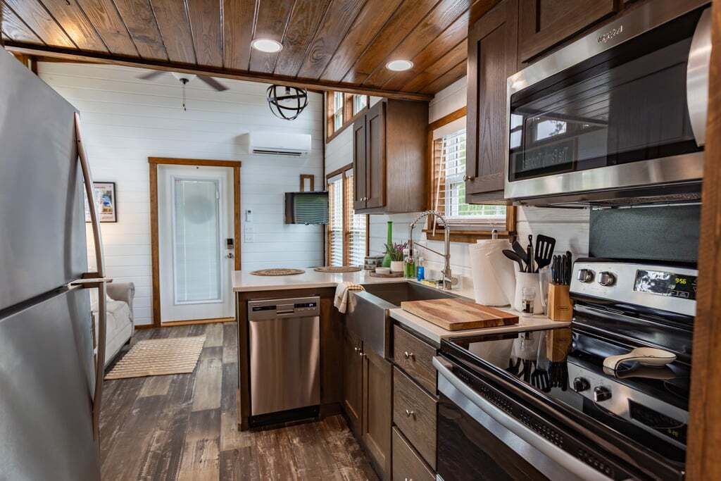 A compact kitchen with wooden cabinets, a stainless steel refrigerator, a dishwasher, and a built-in oven.