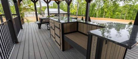 Una terraza al aire libre con piso de madera, una zona de bar integrada y un espacio de estar techado.