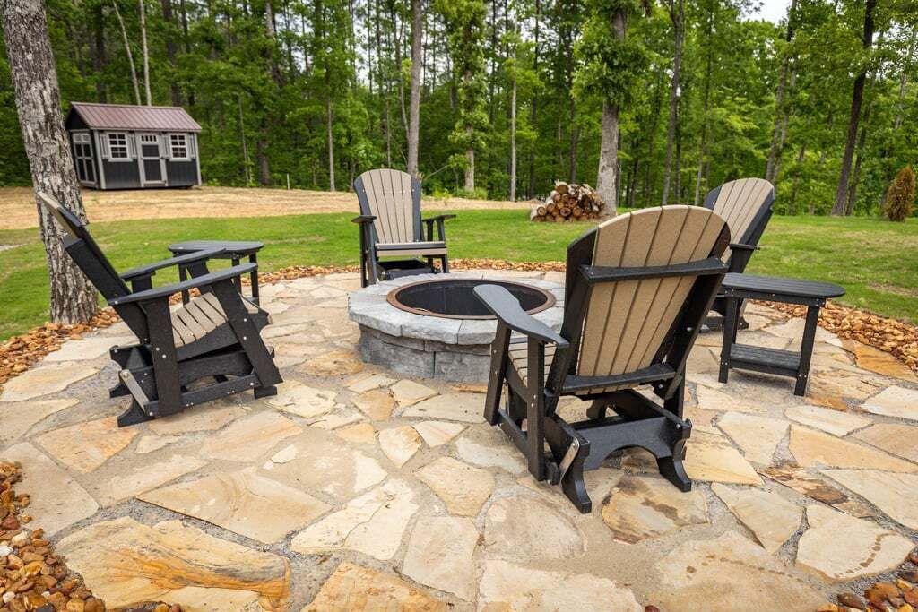 A stone patio with Adirondack chairs and a fire pit.