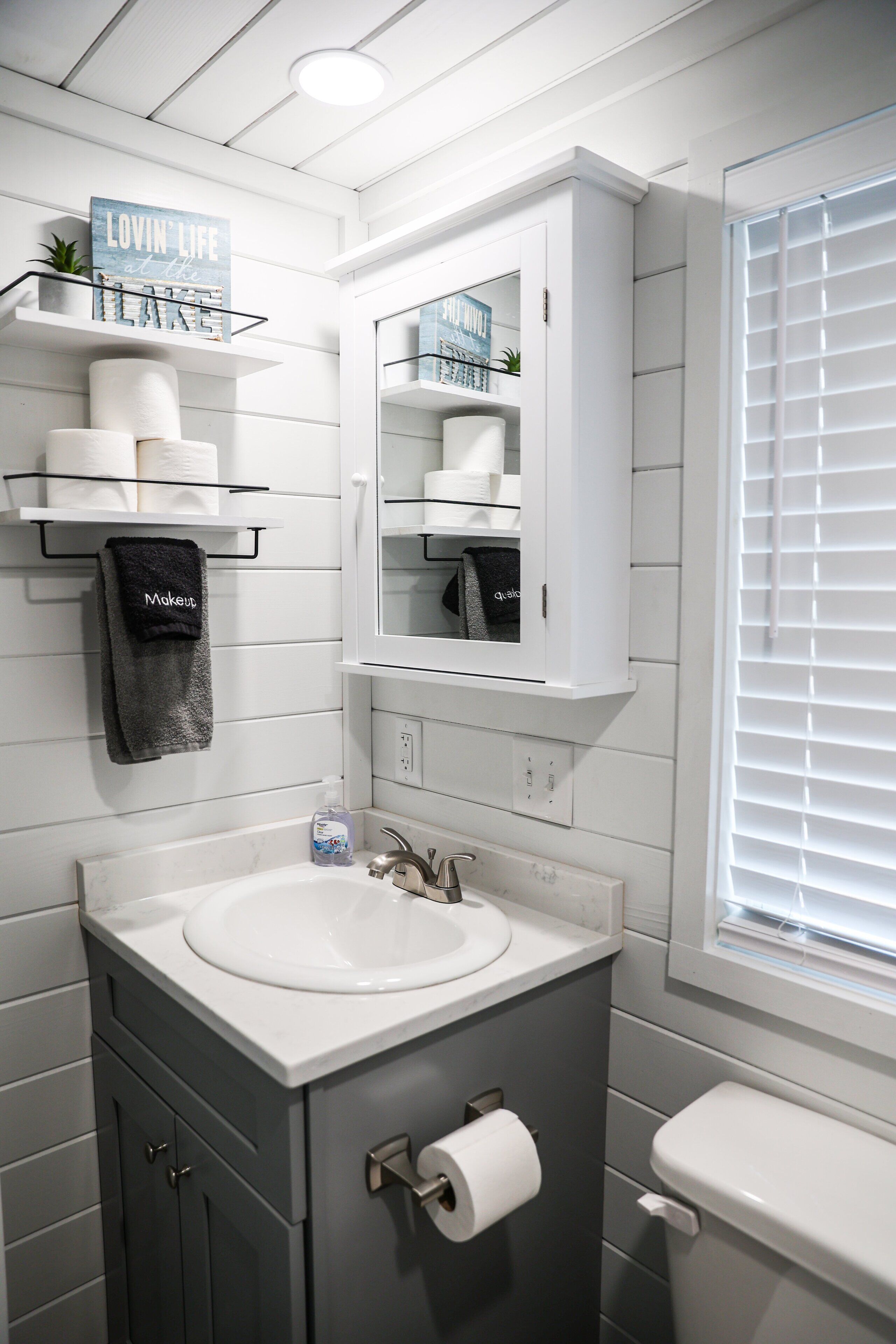 Une salle de bain moderne avec un meuble-lavabo blanc, un évier, des toilettes et une fenêtre équipée de stores.