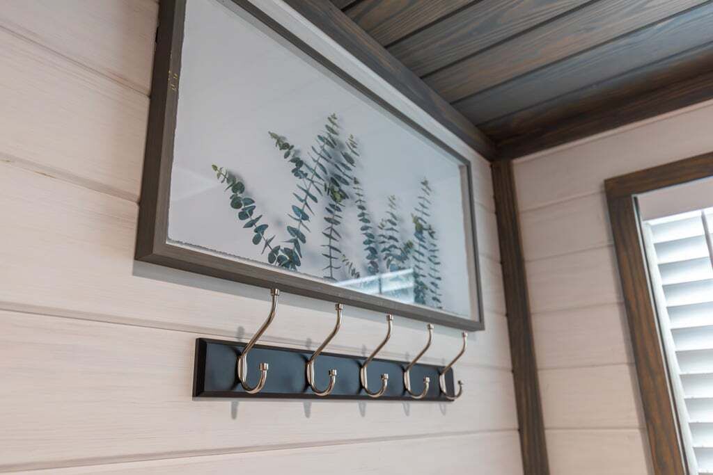 A wall-mounted picture frame with a botanical print and a black metal coat hook below it.
