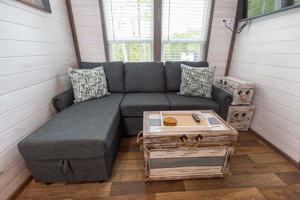 A cozy room with a grey sectional sofa, patterned pillows, and a wooden chest with drawers.