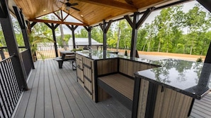 Una terraza al aire libre con piso de madera, una zona de bar integrada y un espacio de estar techado.
