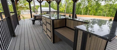 En udendørs terrasse med trægulv, en indbygget bar og et overdækket siddeområde.