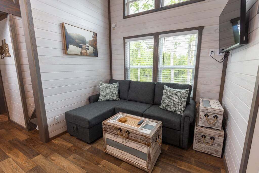 Une pièce chaleureuse avec un canapé d’angle gris, une commode en bois et un tableau accroché au mur.