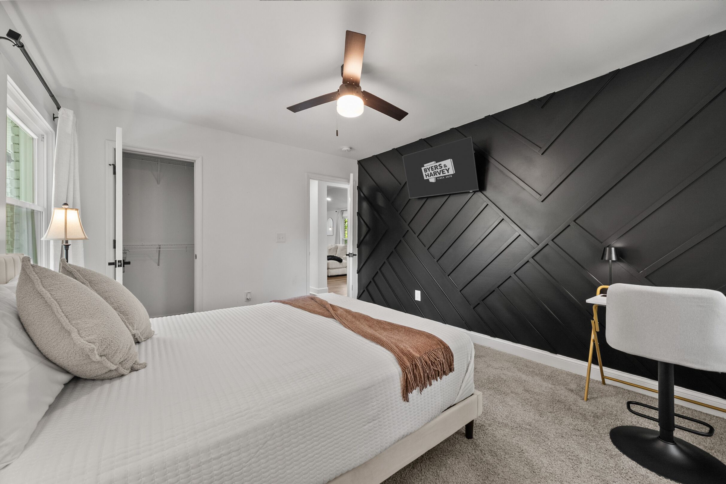 A modern bedroom with a bed, a ceiling fan, a black accent wall, and a small table with a chair.