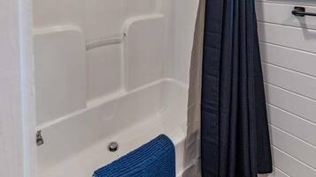 Een badkamer met een bad, douchegordijn en een raam.