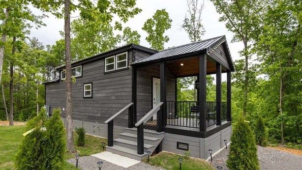 A two-story cabin with a porch, a staircase, and a gravel driveway. - The Nesting Nook (Dover)