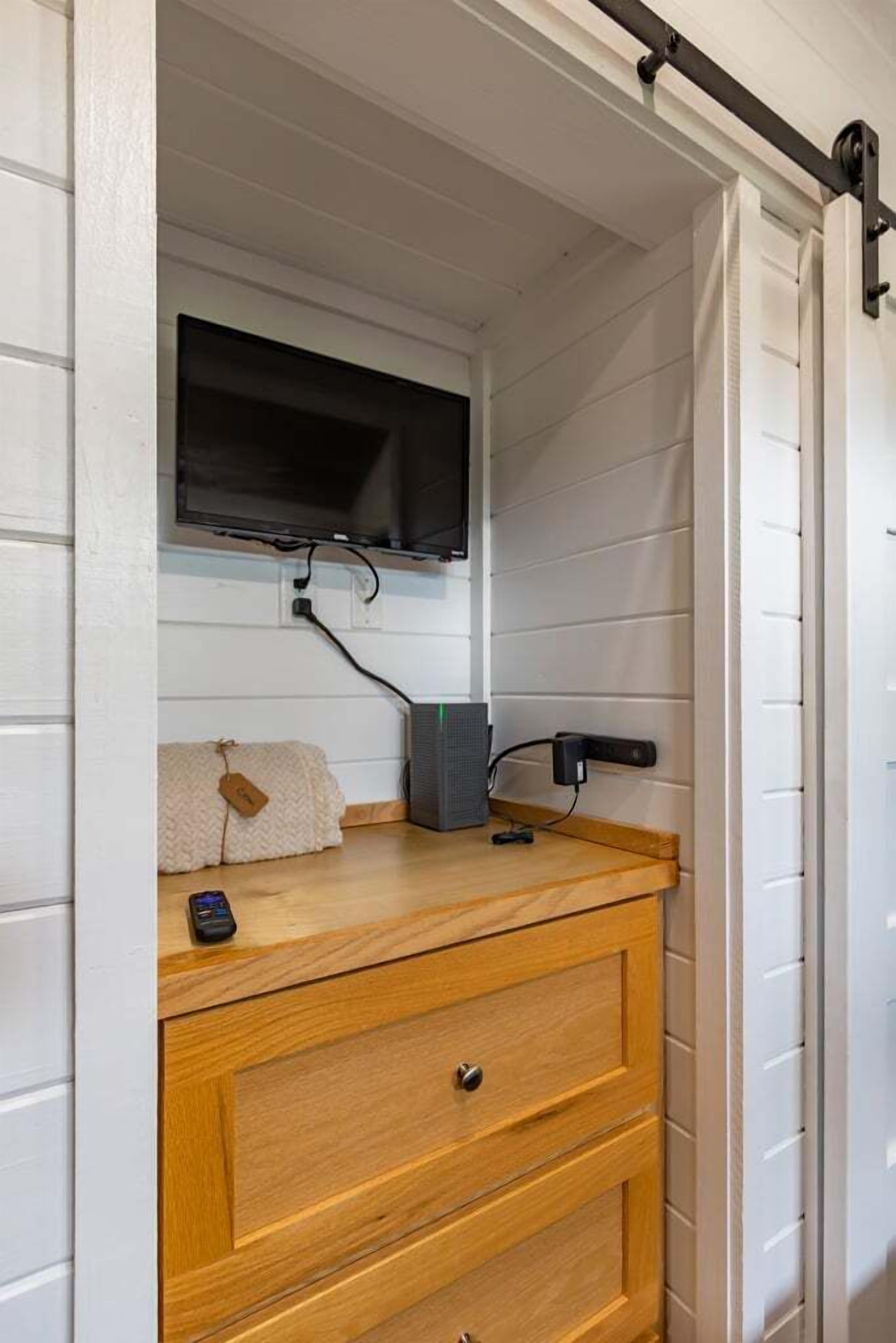 Una stanza con un comò in legno, una televisione fissata al muro e una porta scorrevole.