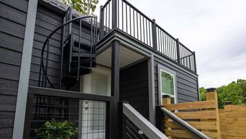 Un bâtiment à deux étages doté d’une terrasse en bois, d’un escalier en colimaçon et d’un espace clos agrémenté de plantes.