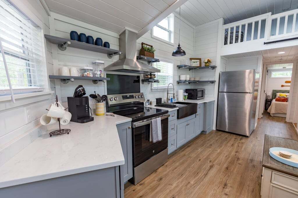 A modern kitchen with white cabinetry, stainless steel appliances, and a wooden floor.