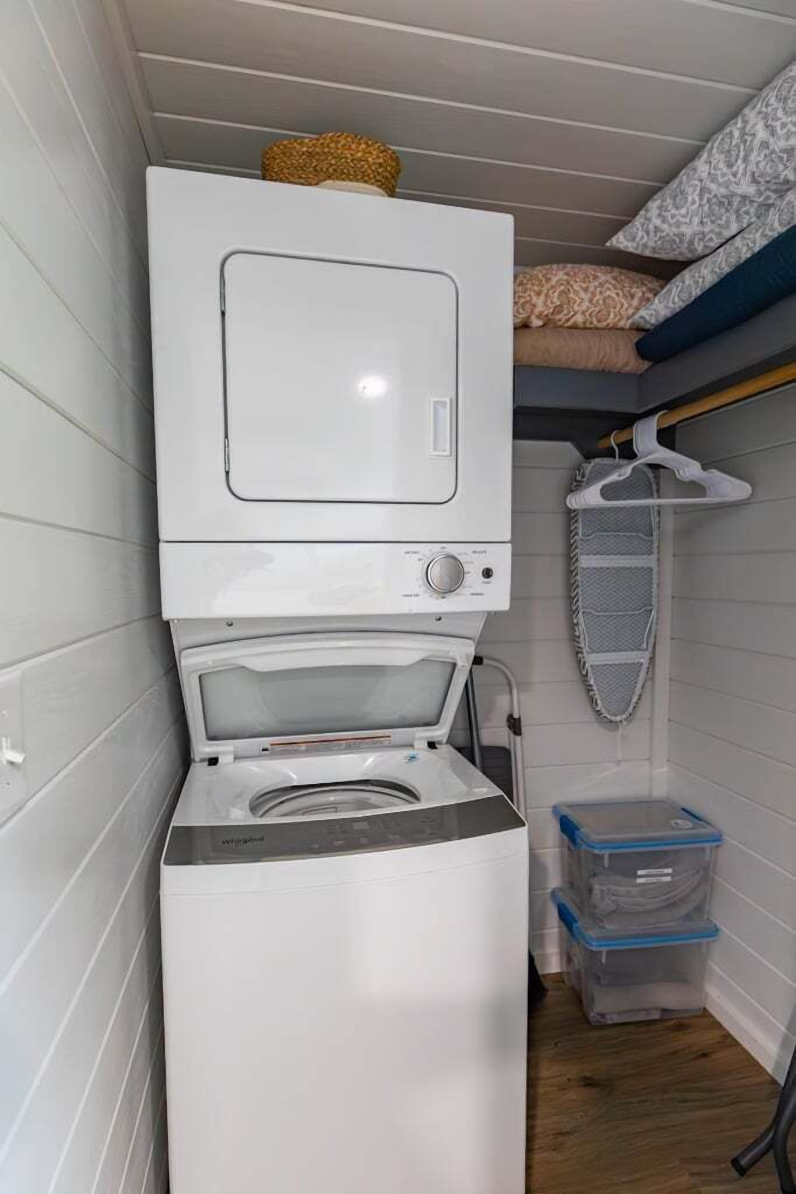 A compact laundry room with a stacked washer and dryer, a drying rack, and storage bins.