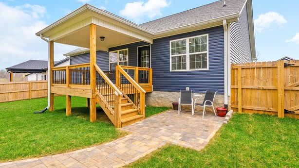 Ein Wohnhaus mit überdachter Veranda, einer Holztreppe und einer Terrasse mit Gartenmöbeln.