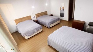 A room with three beds, wooden flooring, a small desk, and a mirror on the wall. - Camber Inn Hotel (Mancora)