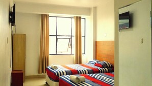 A hotel room with two beds, a TV, a desk, and a window with curtains. - Camber Inn Hotel (Mancora)