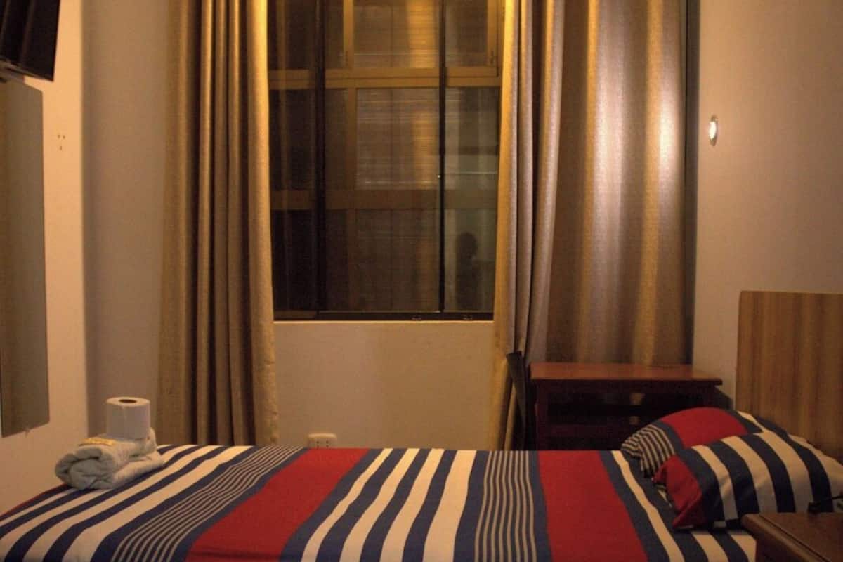 Una habitación de hotel con una cama, una ventana con cortinas, un escritorio y una silla.