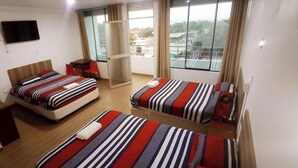 A hotel room with two beds, a TV, a balcony, and a view of the city. - Camber Inn Hotel (Mancora)