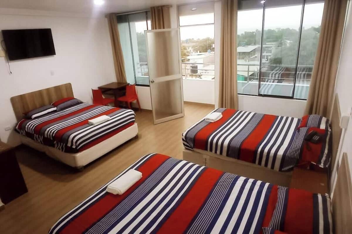 Habitación de hotel con dos camas, televisión, balcón y vista a la ciudad.