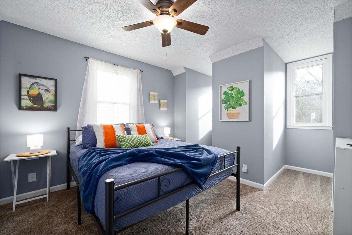 A bedroom with a bed, a ceiling fan, a window, and a small bedside table.