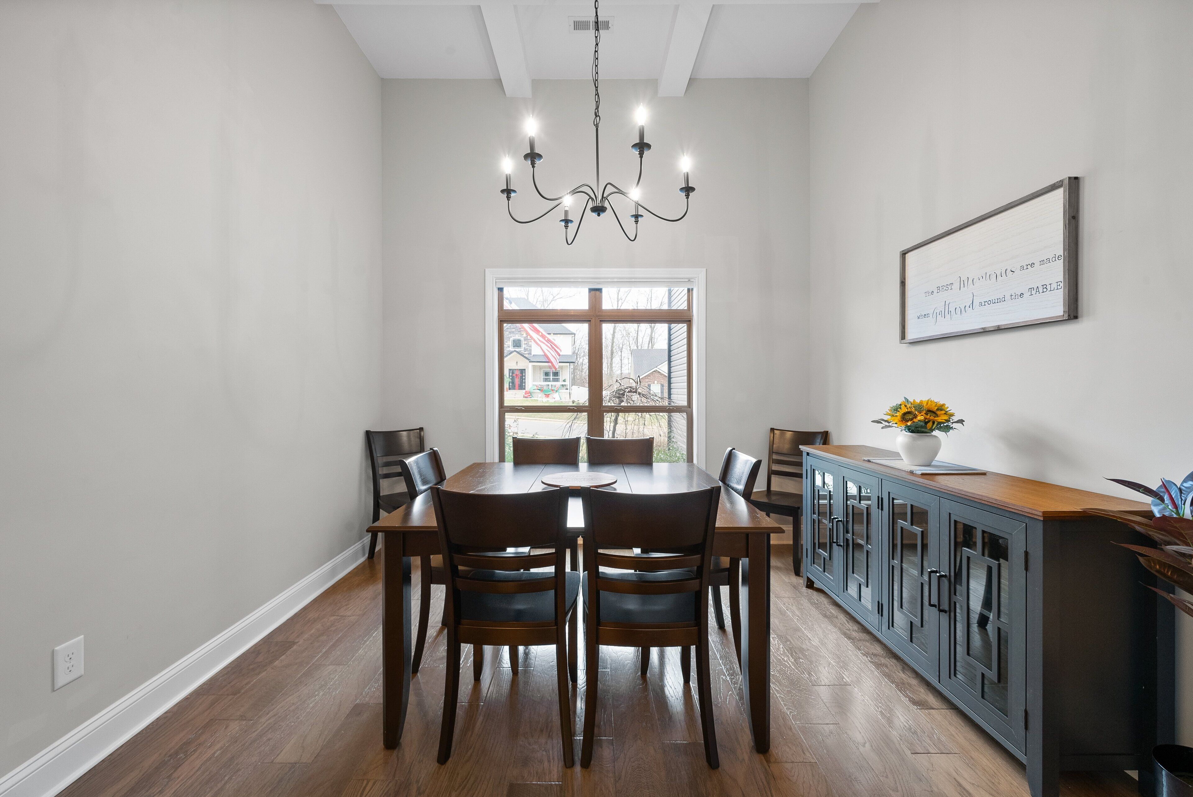 A dining area with a wooden table and chairs, a chandelier, a cabinet with drawers, and a window with a view of a building outside.