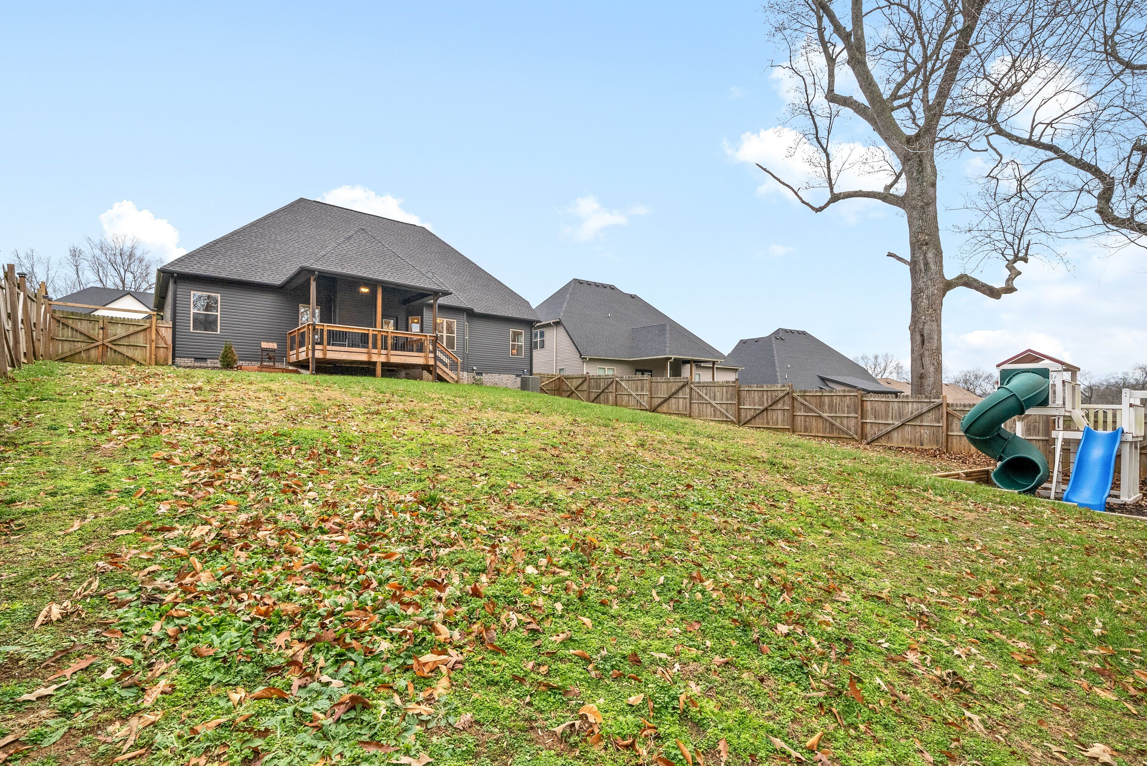 A residential area with houses, a grassy slope, a wooden deck, and a playground structure.