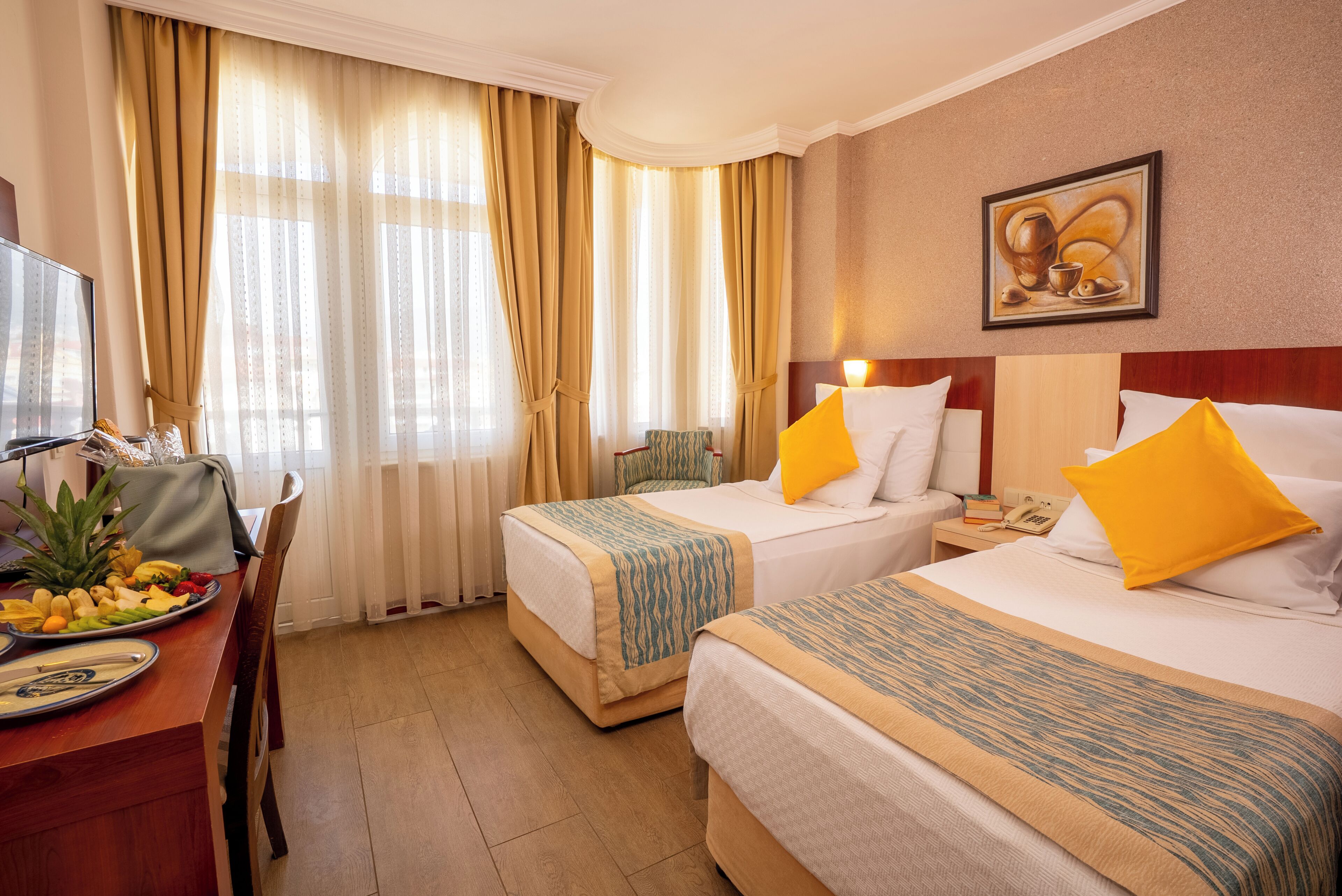 A hotel room with two beds, a desk with breakfast, and a painting on the wall.