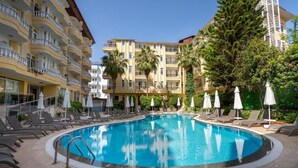 Una piscina con sillones de descanso y sombrillas, rodeada de edificios de varios pisos con balcones.