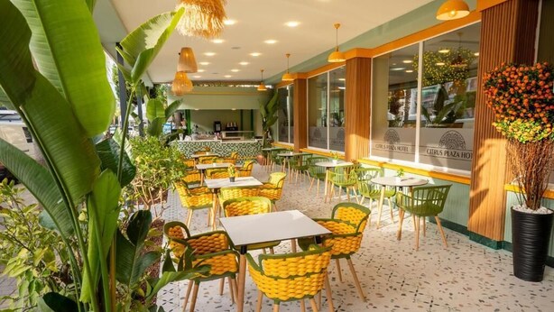 Un restaurante con terraza, que incluye mesas y sillas, rodeado de plantas grandes y un arreglo floral decorativo.