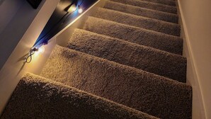 A carpeted staircase with string lights, framed artwork on the walls, and a large black sign with white letters. - Kim's Place on Cigar Hill (Clarksville)