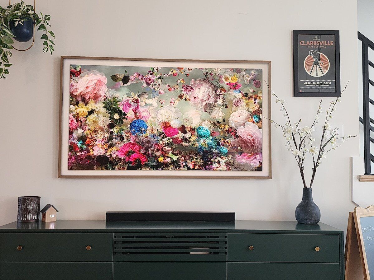 A framed floral artwork on a wall above a dark green dresser with drawers.