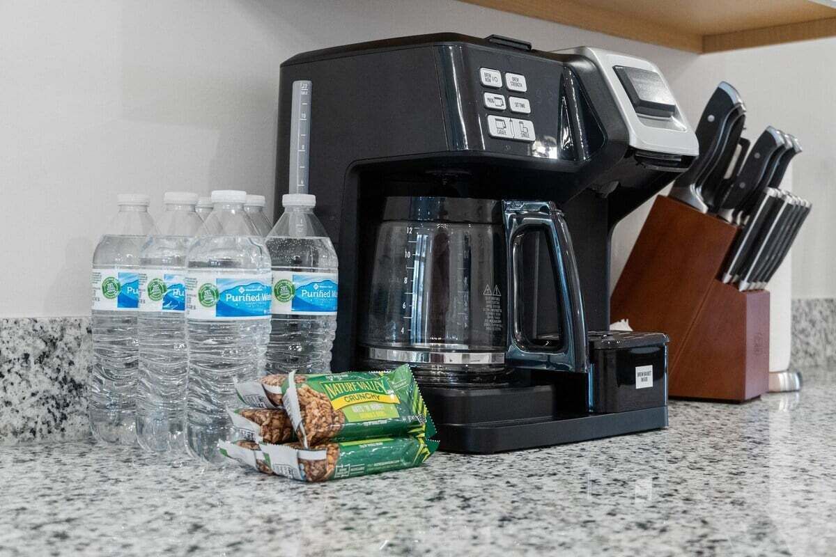 A coffee maker, water bottles, and a snack package on a kitchen counter.