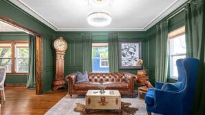 Ein Zimmer mit einem braunen Ledersofa, einem blauen Sessel, einem Holznachttisch, einer Vintage-Uhr und einem großen gerahmten Bild an der Wand.