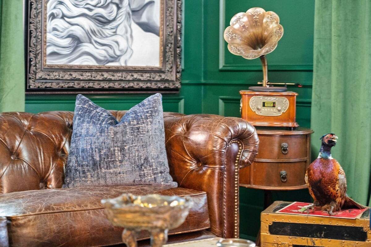 A leather sofa with a blue pillow, a gramophone, and a pheasant on a chest of drawers.