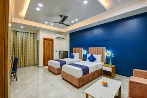 A hotel room with two beds, a ceiling fan, an air conditioning unit, a wooden door, a small table with a vase of flowers, and a chair.