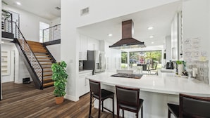 A modern kitchen with a large island, wooden staircase, and a potted plant.