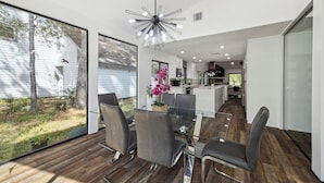 A modern kitchen with a central island, a dining area with a glass table and chairs, and a view of the backyard.