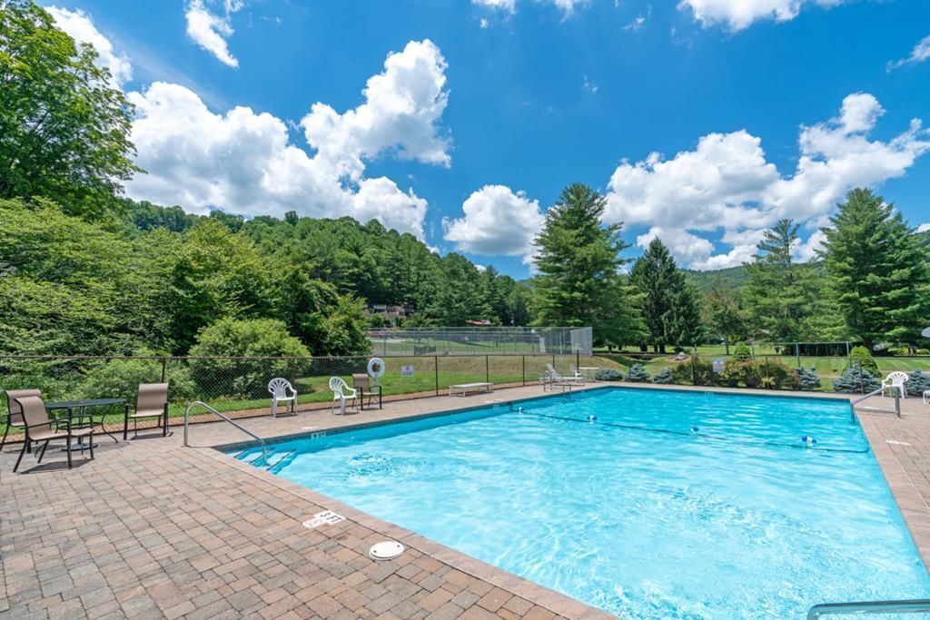 A rectangular swimming pool with a brick deck, surrounded by lounge chairs and a fence.