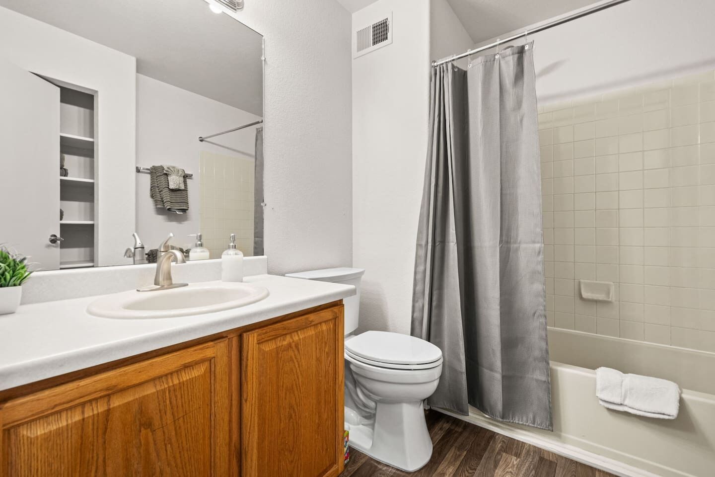 A modern bathroom with a white sink, wooden vanity, a toilet, and a shower with a grey curtain.