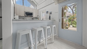 Een keuken met witte kastjes, een magnetron en een bar met krukken.