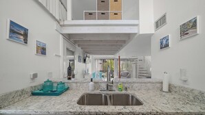 Een keuken met een dubbele spoelbak, witte kastjes en een marmeren aanrecht. Er hangen rieten manden aan de muur en is uitzicht op buiten.