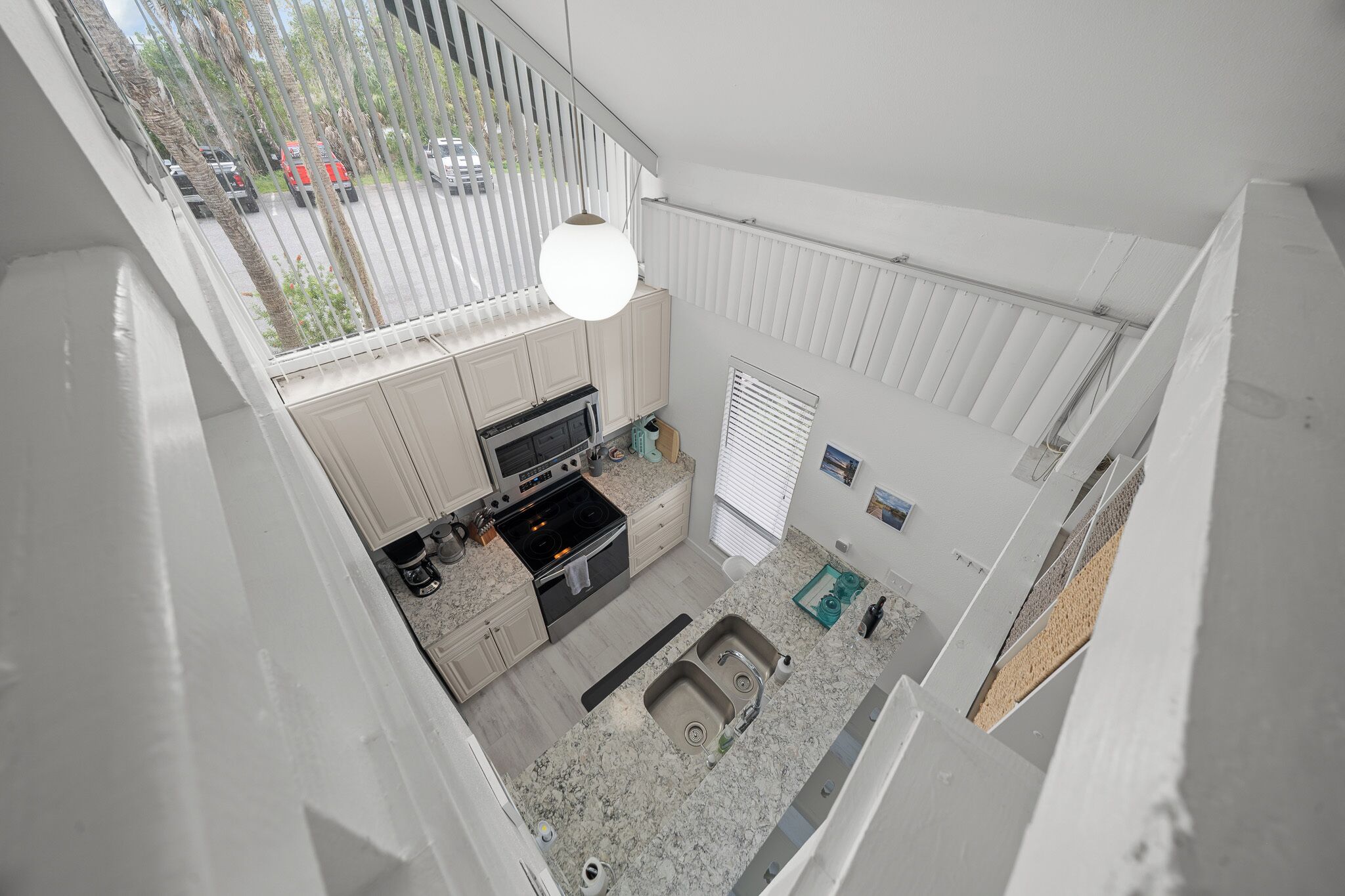 A kitchen with a built-in oven, a sink, and a window overlooking a parking area.
